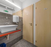 Badezimmer in Geschäftsräumen mit Waschbecken, zwei Holztüren und Fliesen.
