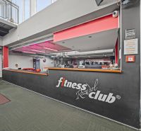 Rezeption eines Fitnessstudios mit einem Schild, roter Beleuchtung und dekorativen Trophäen auf einem grünen Boden.
