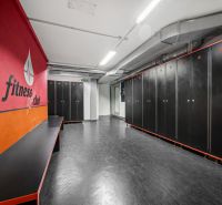 Fitness-Umkleideraum mit schwarzen Schließfächern und roter Wand in Geschäftsräumen.