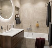 Badezimmer mit Badewanne, hängendem Waschbecken und rundem beleuchtetem Spiegel in einer 2-Zimmer-Wohnung.