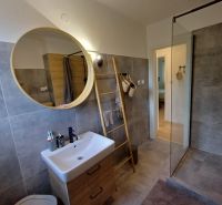 Badezimmer in einer 2-Zimmer-Wohnung mit Duschkabine, Waschbecken und rundem Spiegel.