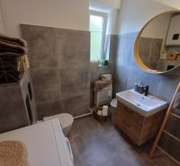 Badezimmer in einer 2-Zimmer-Wohnung mit rundem Spiegel und praktischem Stauraum.