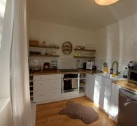 Küche in einer 2-Zimmer-Wohnung mit weißer Küchenzeile und Boden in Holzoptik.