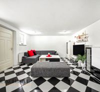 Wohnzimmer in einem Einfamilienhaus mit schwarz-weißem Schachbrettboden und grauem Sofa.