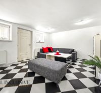 Wohnzimmer in einem Einfamilienhaus mit Schachbrettboden und grauen Sitzmöbeln.