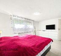 Helles Schlafzimmer mit roter Decke, Fernseher an der Wand und Holzboden.