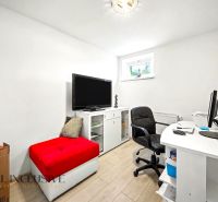 Ein Arbeitszimmer in einem Einfamilienhaus mit weißen Möbeln und einem roten Hocker.