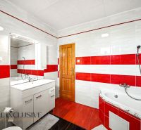 Das Badezimmer eines Einfamilienhauses mit roten und weißen Fliesen, einer Eckbadewanne und Schränken.
