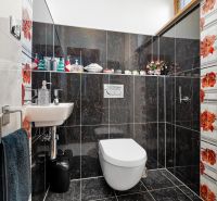 Ein Badezimmer in einem Einfamilienhaus mit dunklen Fliesen und bunten Blumenmotiven.