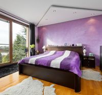 Ein Schlafzimmer in einem Einfamilienhaus mit einer lila Wand, einem Bett und einem Boden in Holzoptik.