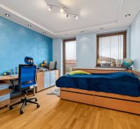 Kinderzimmer mit blauer Wand, Bett, Schreibtisch und Boden in Holzoptik.