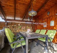 Ein Holzpavillon mit Steinboden und grünen Stühlen bei einem Einfamilienhaus.