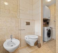 Badezimmer mit Toilette, Bidet und Waschmaschine in einem Einfamilienhaus. Cremefarbene Fliesen und Bodenbelag.