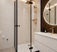 Badezimmer in einer 3-Zimmer-Wohnung mit eleganter Dusche, goldenen Details und beleuchtetem Spiegel.