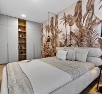 Schlafzimmer in einer 2-Zimmer-Wohnung mit Holzboden und Tapete mit exotischem Motiv.