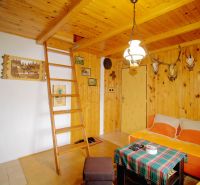 Holzinterieur der Hütte mit Leiter und Kaminofen, ergänzt durch Jagddekor.