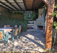 Überdachte Terrasse mit Kamin neben einer Hütte bei Žilina, umgeben von Grün und Sitzgelegenheiten.