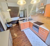 Küche mit orangefarbener Küchenzeile, Sofa und Boden mit Holzdekor in einer 3-Zimmer-Wohnung.