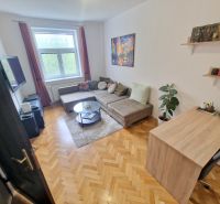 Ein Zimmer in einer 3-Zimmer-Wohnung mit einem Sofa, einem Fernseher und einem Boden in Holzoptik.