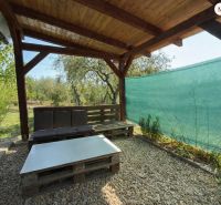 Eine hölzerne Pergola mit Sitzgelegenheit in einer Hütte im Weingarten in Lučenec, umgeben von Grün.