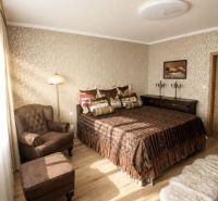 Schlafzimmer mit Sessel und Bett, Holzboden, warme Farbtöne.