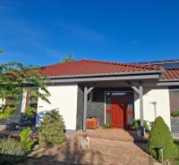 Ein Einfamilienhaus in Nové Zámky mit rotem Dach, Solarpaneelen und Garten.