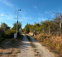 Ein befestigter Feldweg, der zur Hütte in Banka führt, gesäumt von Büschen und einem Zaun.
