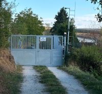 Das Tor, das zur Hütte in Banka führt, umgeben von Grün und einem Feldweg.