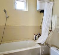 Badezimmer mit Badewanne, Dusche, Boiler und Boden mit Holzdekor in einem Einfamilienhaus.