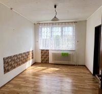 Ein Zimmer in einem Einfamilienhaus mit einem Boden in Holzoptik, einem Vorhang und einem Heizkörper unter dem Fenster.