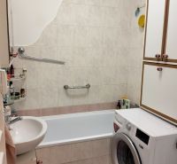 Badezimmer in einer Einzimmerwohnung mit Badewanne und Waschmaschine, gefliest mit hellen Fliesen.