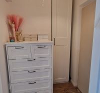 Ein Zimmer in einer Einzimmerwohnung mit einer Kommode, einem Kleiderschrank und einem Boden in Holzoptik.