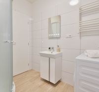 Badezimmer in einem Studio-Apartment mit Holzboden, weißen Fliesen und einer Duschkabine.