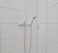 Duschkabine mit weißen Fliesen und Duschkopf in einem Einzimmerapartment.