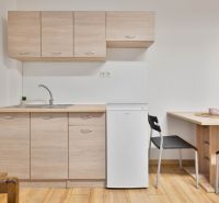 Küchenbereich in einem Einzimmerapartment mit weißem Kühlschrank und Holzboden.
