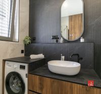 Badezimmer einer Zweizimmerwohnung mit Waschbecken, Waschmaschine und Spiegel.