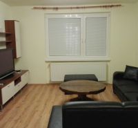 Wohnzimmer in einer 3-Zimmer-Wohnung mit Holzdekorboden und schwarzem Sofa.