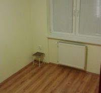 Ein Zimmer in einer 3-Zimmer-Wohnung mit einem Boden in Holzoptik und weißen Fenstern.