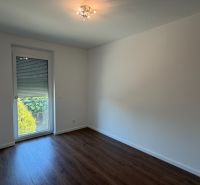 Ein Zimmer in einer 3-Zimmer-Wohnung mit weißen Wänden und einem Boden in Holzoptik.