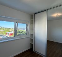 Ein Zimmer mit einem Einbauschrank, einem Boden in Holzoptik, einem großen Fenster mit Ausblick.