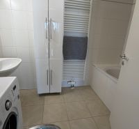 Badezimmer in einer 3-Zimmer-Wohnung mit Waschmaschine, Waschbecken und Badewanne auf hellen Fliesen.