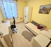 Ein gelbes Zimmer mit einem Einzelbett, einem Schreibtisch und einem Boden in Holzoptik in einer Vierzimmerwohnung.