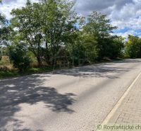 Eine Straße in Bernolákovo, umgeben von Grünflächen auf landwirtschaftlichen und forstwirtschaftlichen Grundstücken, blauer Himmel.