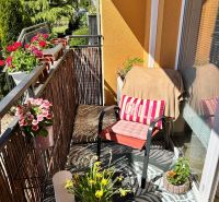 Balkon einer 3-Zimmer-Wohnung mit bequemen Sitzgelegenheiten, Blumen und Blick ins Grüne.