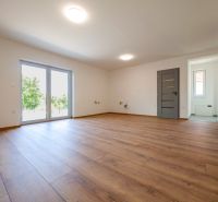 Wohnzimmer in einem Einfamilienhaus mit großen Fenstern und einem Boden in Holzoptik.
