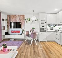 Wohnzimmer in einem Einfamilienhaus mit Küche, weißen Möbeln und einem Boden in Holzoptik.