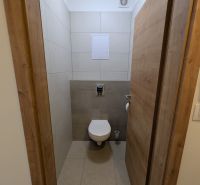 Toilette in einer 2-Zimmer-Wohnung mit Keramikfliesen und einem Boden in Holzoptik.