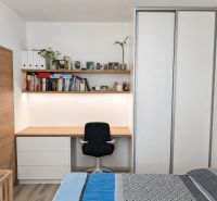 Schlafzimmer in einer 2-Zimmer-Wohnung mit Arbeitsecke, Büchern und Boden in Holzoptik.