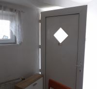 Eingangstür in einer 2-Zimmer-Wohnung mit Holzdekor der Kommode und des Stuhls.