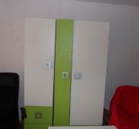 Ein Kleiderschrank mit bunten Türen und ein schwarzer Sessel in einer Zweizimmerwohnung.